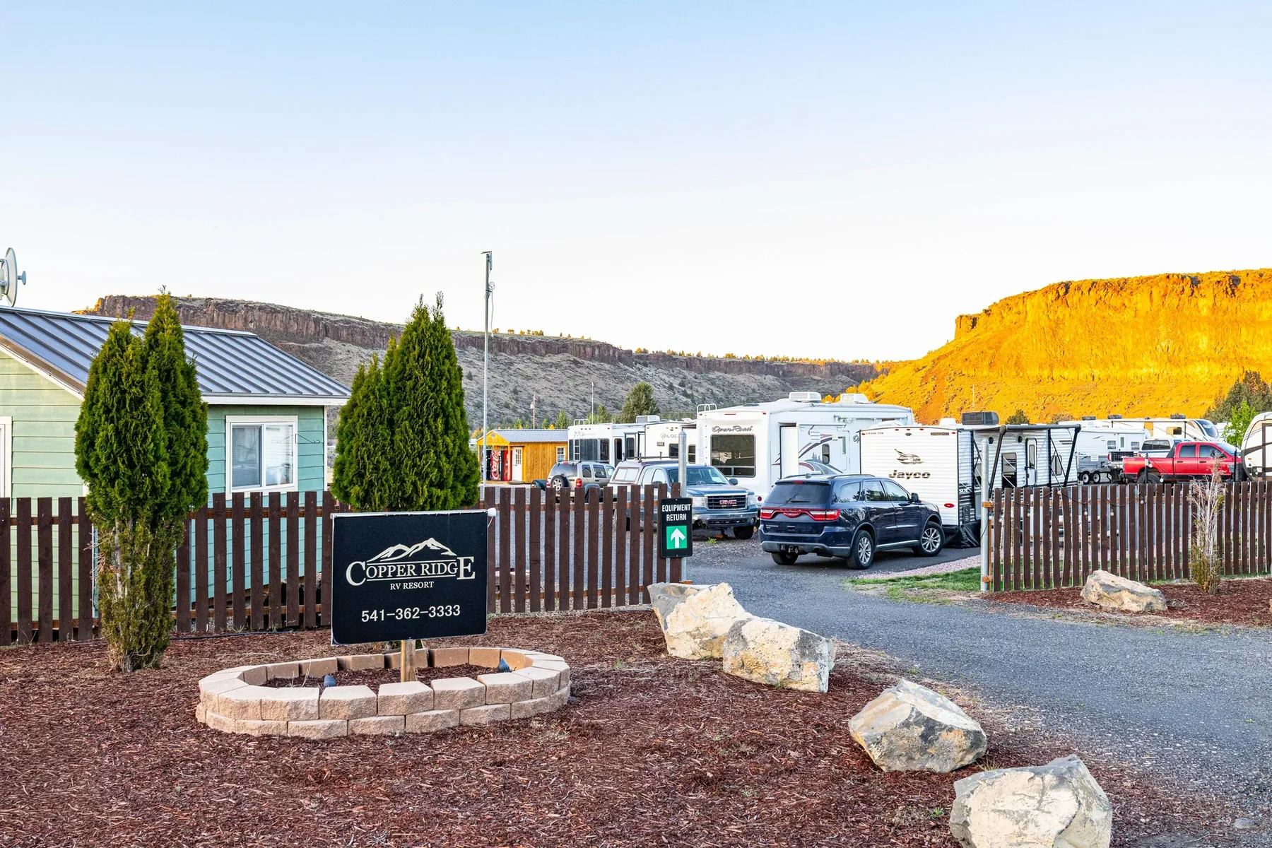 Copper Ridge RV Resort entrance sign at golden hour with RVs and glowing canyon wall, Terrebonne Oregon