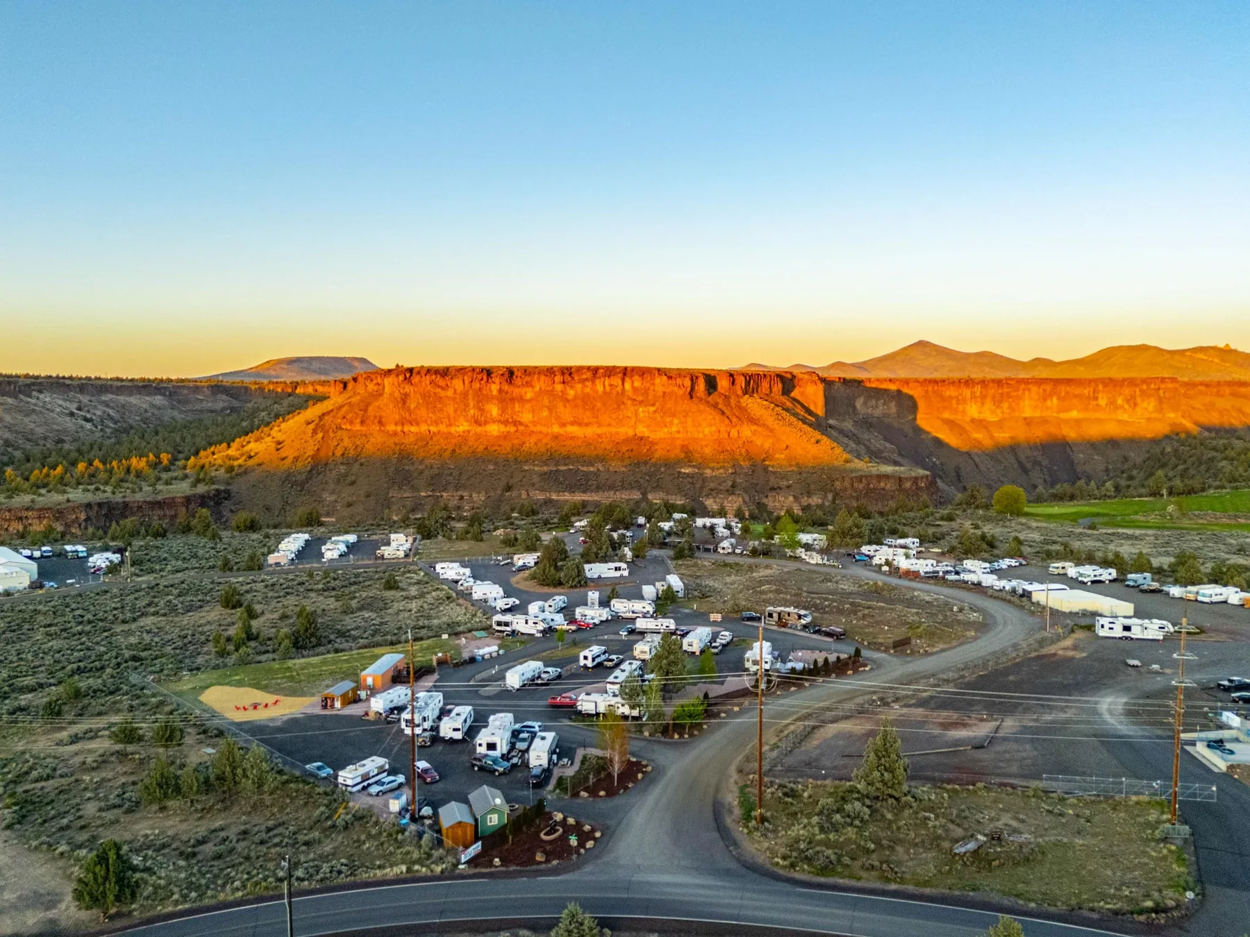 Aerial view of Copper Ridge RV Resort at sunset with Crooked River Canyon glowing orange behind the park, Terrebonne Oregon